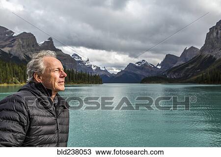 Stock Image - Caucasian man standing near mountain lake. Fotosearch