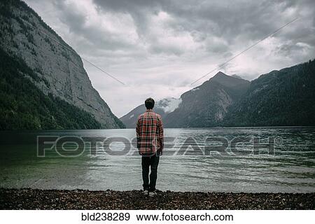 Stock Photo - Caucasian man standing near mountain lake. Fotosearch