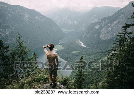 Caucasian man standing on rock overlooking lake in valley View Large Photo Image Stock Photo - Caucasian man standing on rock overlooking lake in valley. Fotosearch