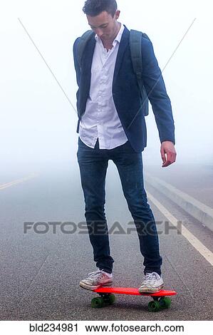 Stock Image - Caucasian man standing on small red skateboard in fog. Fotosearch