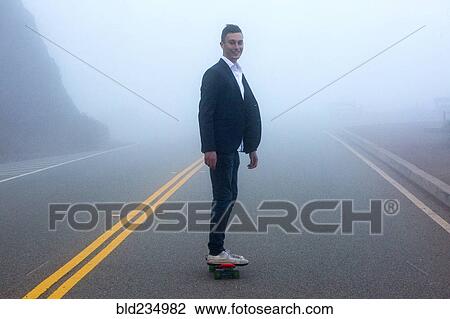 Stock Image - Caucasian man standing on small red skateboard in fog. Fotosearch