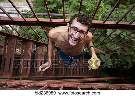 Stock Photo - Caucasian man standing on urban fire escape drinking orange juice. Fotosearch