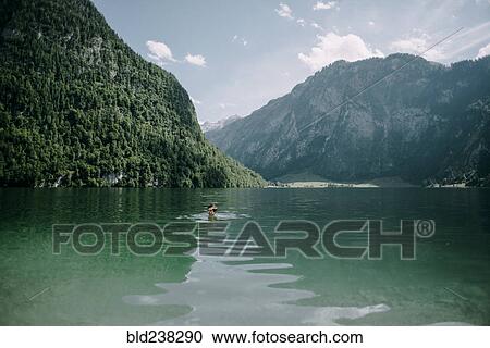 Stock Image - Caucasian man swimming in mountain lake. Fotosearch