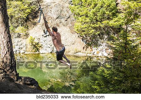 Caucasian man swinging on rope over water View Large Photo Image Stock Image - Caucasian man swinging on rope over water. Fotosearch