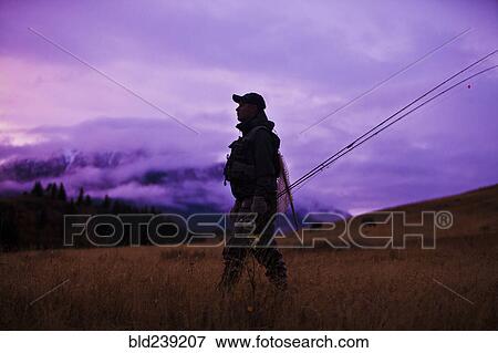 Stock Photo - Caucasian man walking and carrying fishing rods. Fotosearch
