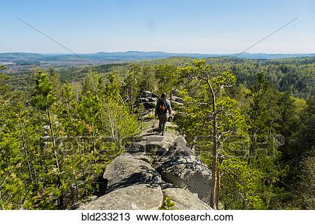 Stock Image - Caucasian man walking on mountain rock admiring scenic view. Fotosearch