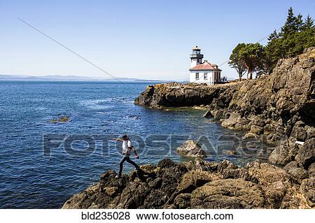 Stock Photo - Caucasian man walking on rocks near lighthouse. Fotosearch