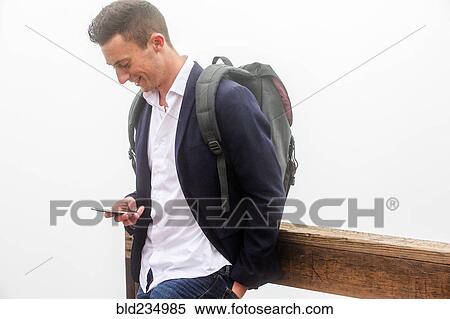 Stock Photography - Caucasian man wearing backpack texting on cell phone. Fotosearch
