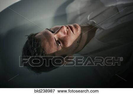 Stock Photo - Caucasian man wearing shirt floating in bathtub water. Fotosearch