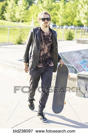 Stock Photo - Caucasian man with beard carrying skateboard. Fotosearch