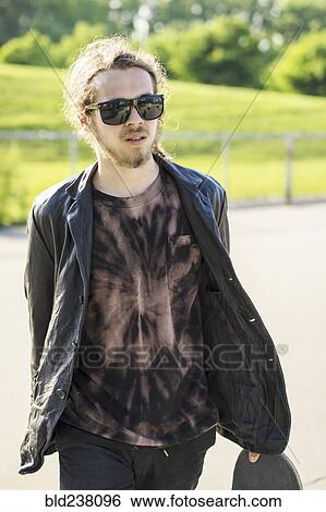 Stock Photograph - Caucasian man with beard carrying skateboard. Fotosearch
