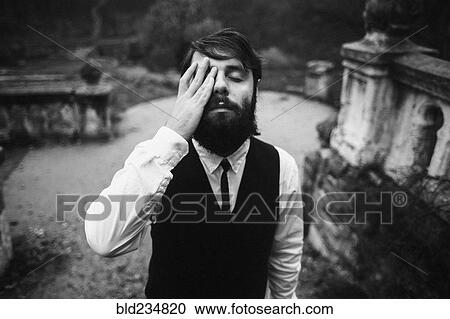 Stock Image - Caucasian man with beard rubbing eye. Fotosearch