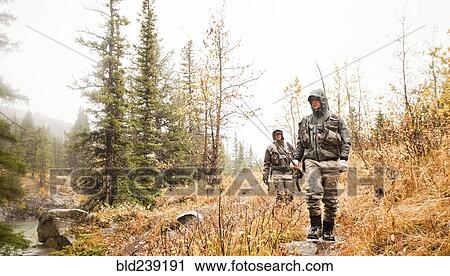 Stock Image - Caucasian men carrying fishing rods. Fotosearch