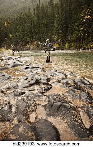 Stock Image - Caucasian men fishing in river. Fotosearch