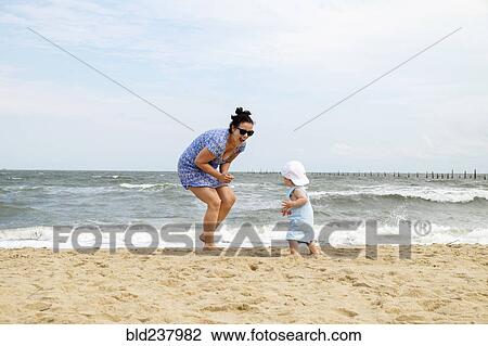 Stock Image - Caucasian mother and baby son playing at beach. Fotosearch