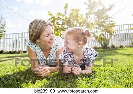 Stock Photo - Caucasian mother and daughter laying in grass. Fotosearch