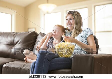 Caucasian mother and daughter sitting on sofa eating bowl of popcorn View Large Photo Image Stock Image - Caucasian mother and daughter sitting on sofa eating bowl of popcorn. Fotosearch