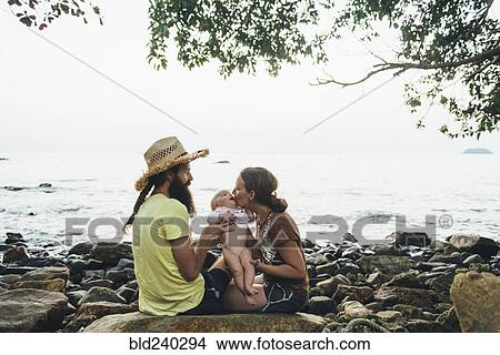 Caucasian mother and father holding baby daughter on rocky beach View Large Photo Image Picture - Caucasian mother and father holding baby daughter on rocky beach. Fotosearch
