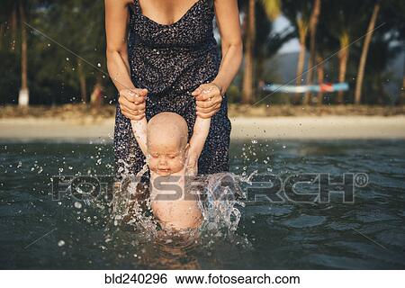 Caucasian mother holding arms of baby daughter splashing in ocean View Large Photo Image Stock Photograph - Caucasian mother holding arms of baby daughter splashing in ocean. Fotosearch
