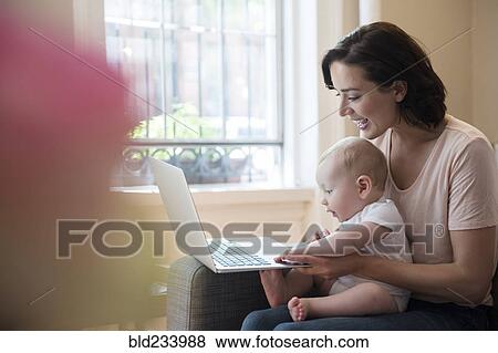 Stock Photo - Caucasian mother holding baby in lap using laptop. Fotosearch