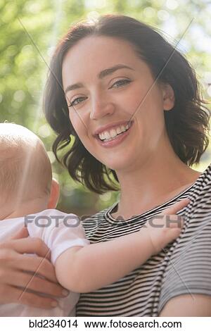 Caucasian mother holding baby son cheek to cheek in sunbeam View Large Photo Image Picture - Caucasian mother holding baby son cheek to cheek in sunbeam. Fotosearch