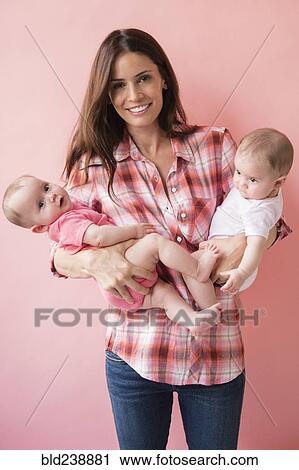 Stock Image - Caucasian mother holding twin baby daughters. Fotosearch