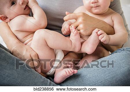 Stock Photograph - Caucasian mother holding twin baby daughters in lap. Fotosearch