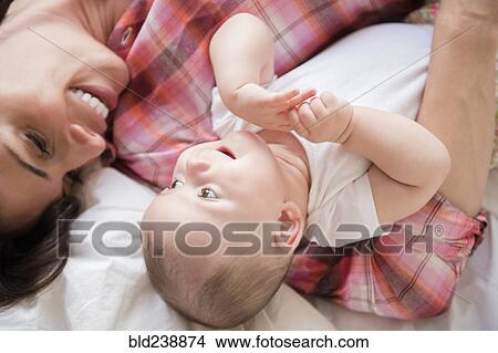 Caucasian mother laying on bed holding baby daughter View Large Photo Image Picture - Caucasian mother laying on bed holding baby daughter. Fotosearch