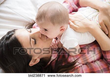 Caucasian mother laying on bed kissing baby daughter View Large Photo Image Stock Image - Caucasian mother laying on bed kissing baby daughter. Fotosearch