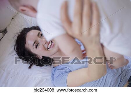 Stock Photo - Caucasian mother laying on bed lifting baby son. Fotosearch