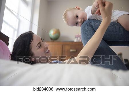 Caucasian mother laying on bed balancing baby son on legs View Large Photo Image Stock Photograph - Caucasian mother laying on bed balancing baby son on legs. Fotosearch