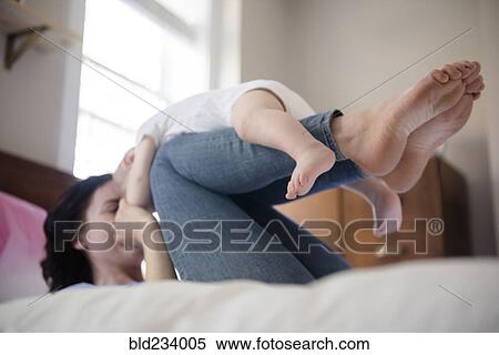 Caucasian mother laying on bed balancing baby son on legs View Large Photo Image Stock Photography - Caucasian mother laying on bed balancing baby son on legs. Fotosearch
