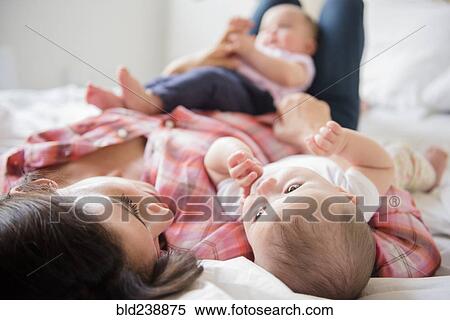 Stock Photography - Caucasian mother laying on bed with twin baby daughters. Fotosearch