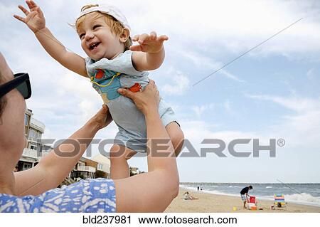 Stock Image - Caucasian mother lifting baby son at beach. Fotosearch