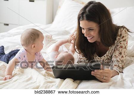 Caucasian mother on bed with twin baby daughters using digital tablet View Large Photo Image Stock Photo - Caucasian mother on bed with twin baby daughters using digital tablet. Fotosearch
