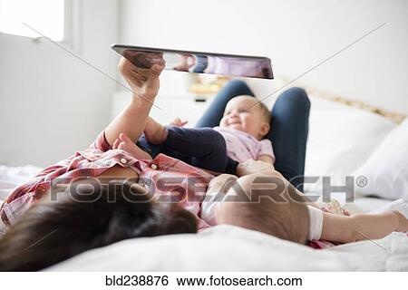 Stock Photograph - Caucasian mother on bed with twin baby daughters using digital tablet. Fotosearch