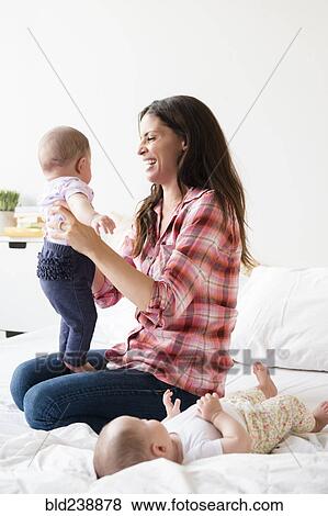 Stock Photo - Caucasian mother playing on bed with twin baby daughters. Fotosearch