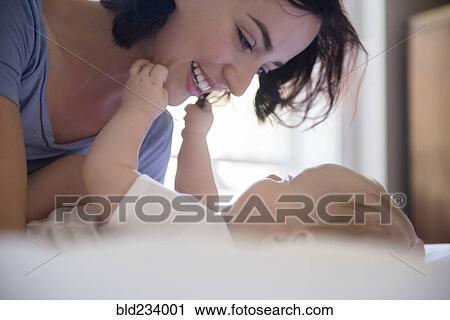 Stock Image - Caucasian mother playing with baby son on bed. Fotosearch