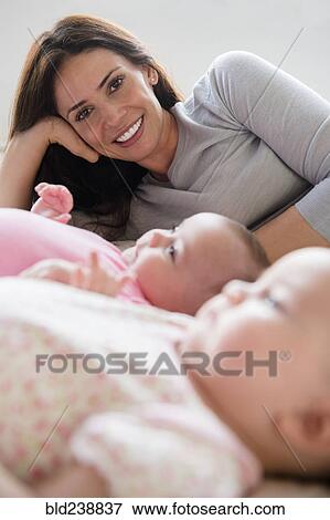 Stock Photo - Caucasian mother posing with twin baby daughters on bed. Fotosearch