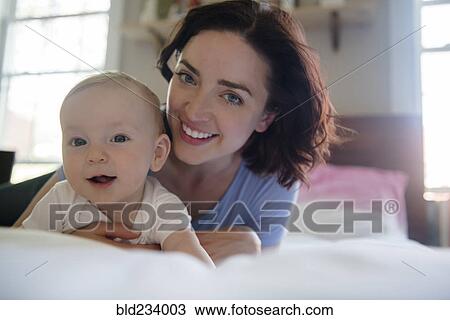 Stock Image - Caucasian mother smiling with baby son on bed. Fotosearch