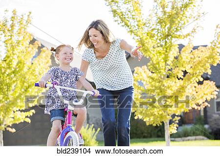Picture - Caucasian mother teaching daughter to ride bicycle. Fotosearch