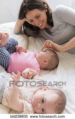 Stock Photography - Caucasian mother touching nose of baby daughter on bed. Fotosearch