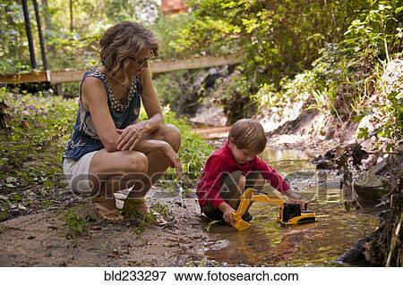 Stock Photo - Caucasian mother watching son playing with construction toys in river. Fotosearch