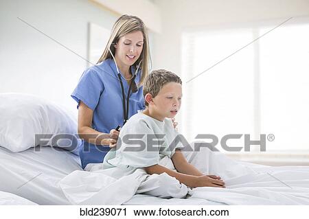 Stock Image - Caucasian nurse listening to chest of boy in hospital bed. Fotosearch