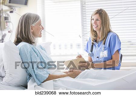 Stock Photo - Caucasian nurse talking with woman in hospital bed. Fotosearch