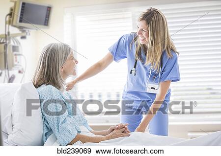 Stock Photo - Caucasian nurse talking with woman in hospital bed. Fotosearch