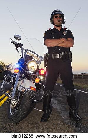 Stock Photo - Caucasian policeman standing near motorcycle. Fotosearch