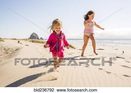 Stock Image - Caucasian sisters running on beach. Fotosearch
