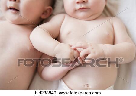 Stock Photo - Caucasian twin baby girls holding hands. Fotosearch