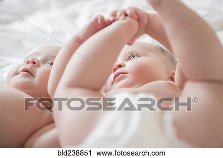 Stock Image - Caucasian twin baby girls laying on bed. Fotosearch